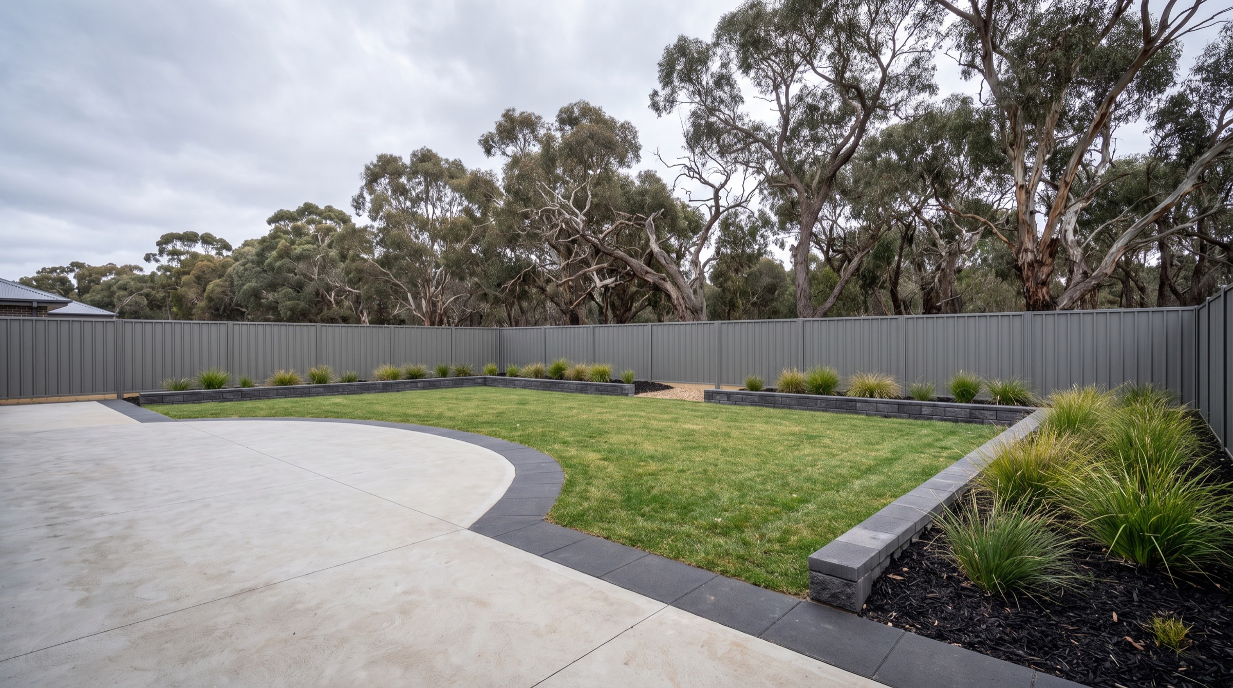 A finished backyard with a broom-finished concrete slab, lawn and block-edged native beds behind a Colorbond fence