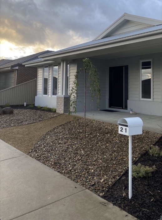 A new home frontage with pebble beds, a young tree and a paved path