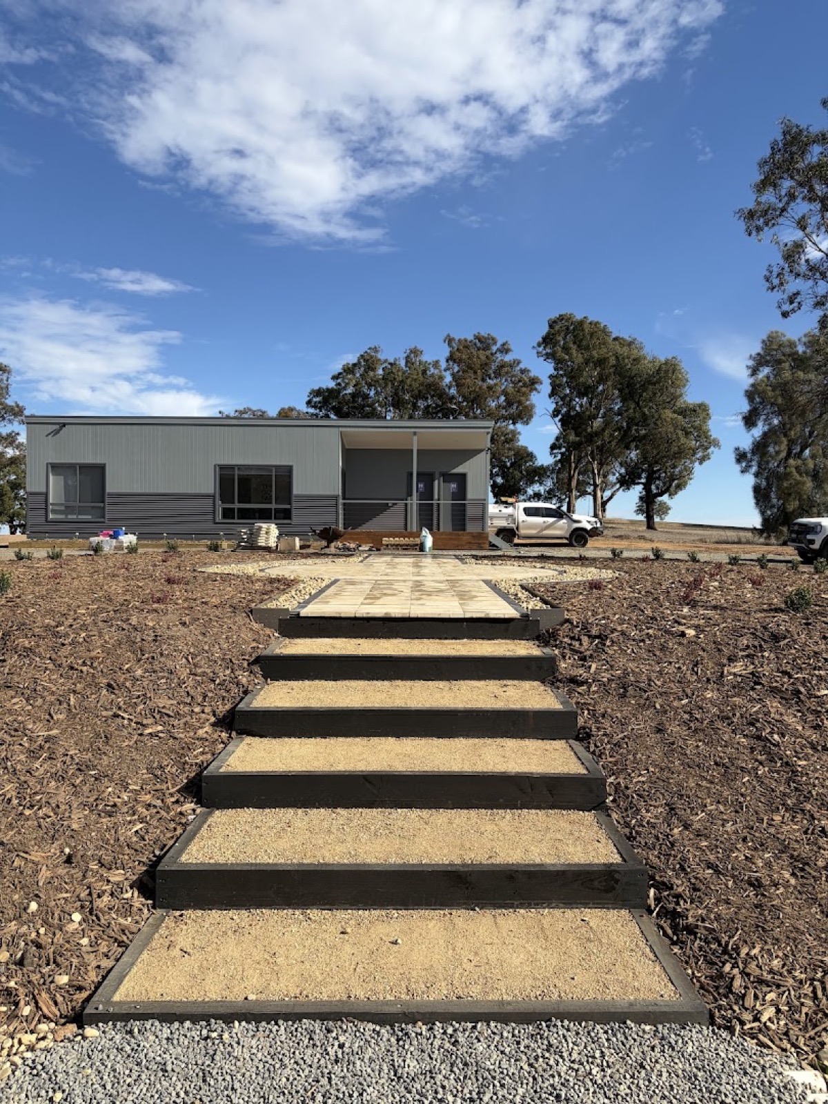 Timber-riser steps set into mulched garden beds leading up to a rural home