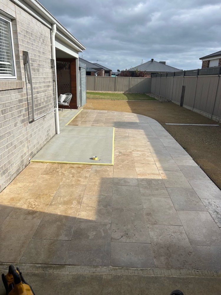 A travertine-paved patio wrapping around the side of a brick home