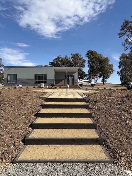 Timber-riser steps set into mulched garden beds leading up to a rural home