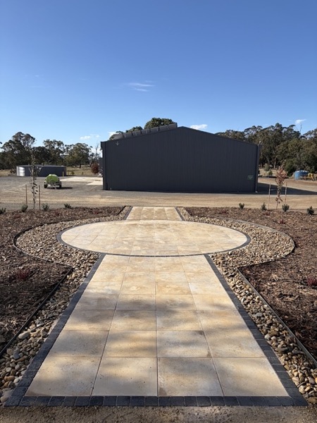 A circular paved entry and path with a cobble border, edged in pebble and mulch
