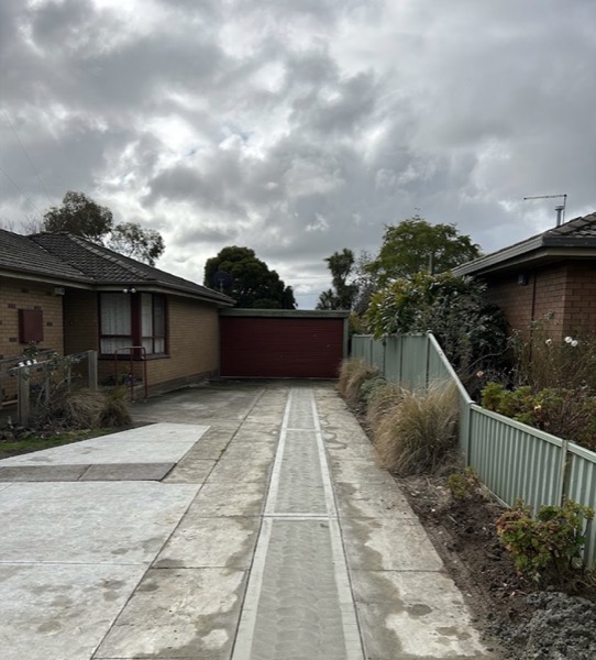 A finished concrete driveway running between two houses to a garage