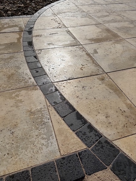 A close view of paving with a curved charcoal cobble border, wet from rain