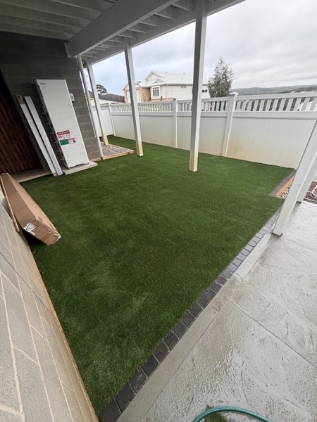 Synthetic turf laid to a paver edge under a pergola, beside a concrete patio